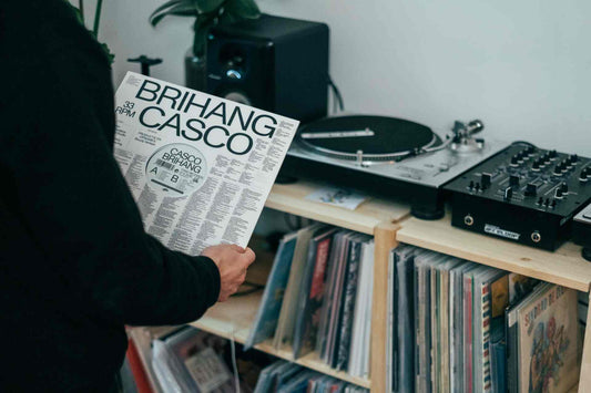 Man holding a vinyl record in front of a player and a record shelf