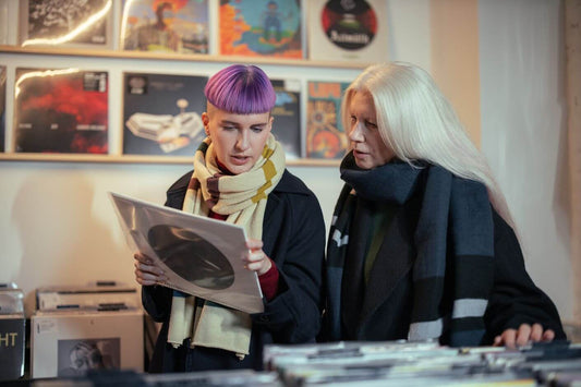 Two individuals talk as they look at an album in a record shop