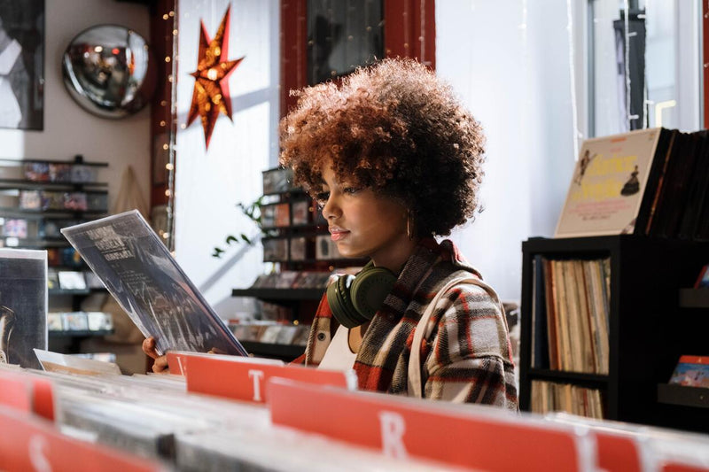 woman with headphones in a red and white plaid shirt collecting vinyl records and shopping at a record store