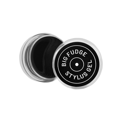 A round silver metal container of Big Fudge Stylus Gel, shown open with the black gel visible inside and the lid placed beside it. The lid features a black label with white text reading 'BIG FUDGE STYlus GEL'.