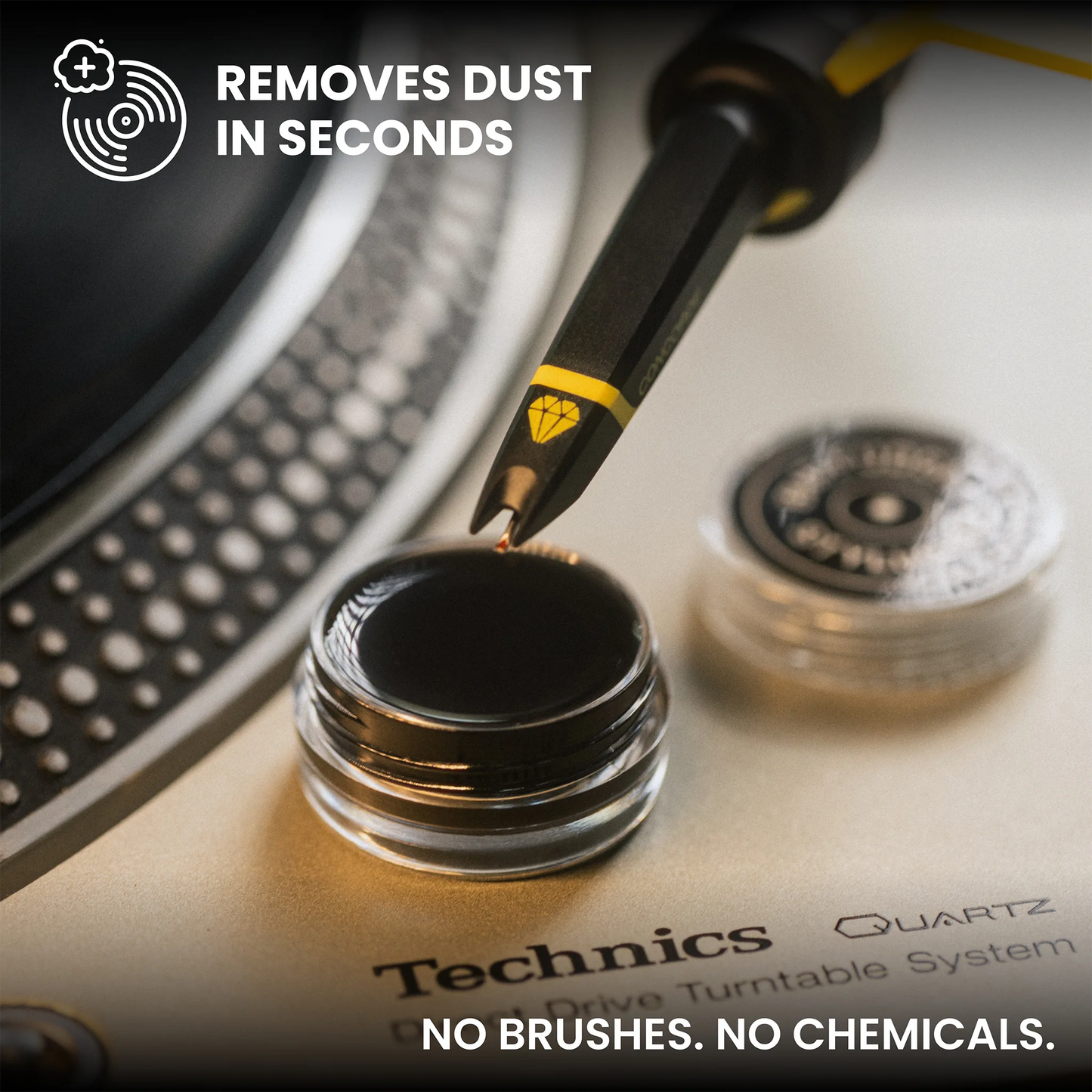 Close-up of a black and yellow anti-static dust remover tool touching a quartz drive turntable surface, with text overlays reading 'REMOVES DUST IN SECONDS' and 'NO BRUSHES. NO CHEMICALS.