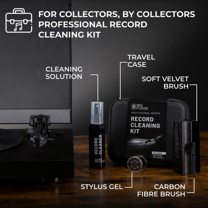 Big Fudge Professional Record Cleaning Kit shown on a wooden surface with a turntable in the background. The kit includes a black travel case, cleaning solution bottle, stylus gel tube, carbon fibre brush, and soft velvet brush, with text labels pointing to each component.