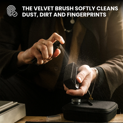 A person holds a small black velvet cleaning brush while spraying a fine mist onto a black case. White text at the top reads, 'THE VELVET BRUSH SOFTLY CLEANS DUST, DIRT AND FINGERPRINTS.