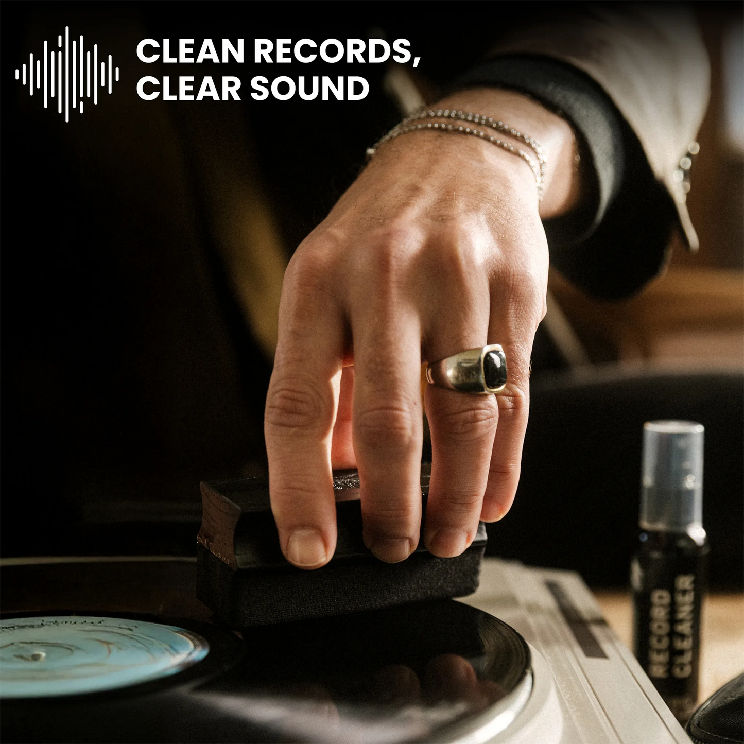 A close-up of a person's hand resting on a vinyl record, with a small bottle labeled 'RECORD CLEANER' nearby. The text 'CLEAN RECORDS, CLEAR SOUND' appears at the top with a soundwave icon.