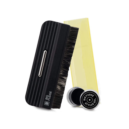 A hair styling brush set on a white background, featuring a black ribbed handle brush with dark bristles, a translucent yellow comb, and a small round black tin labeled 'BFG FUDGE STYLIST'.