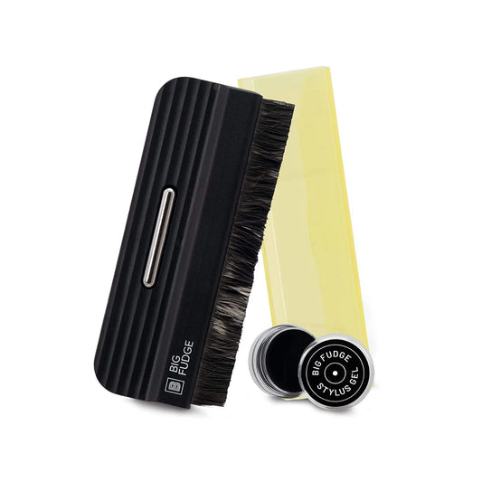 A hair styling brush set on a white background, featuring a black ribbed handle brush with dark bristles, a translucent yellow comb, and a small round black tin labeled 'BFG FUDGE STYLIST'.