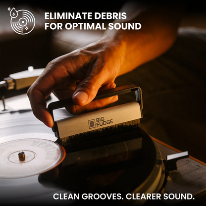 A hand holds a Big Fudge vinyl record cleaning brush over a turntable groove, with text reading 'ELIMINATE DEBRIS FOR OPTIMAL SOUND' and 'CLEAN GROOVES. CLEARER SOUND.