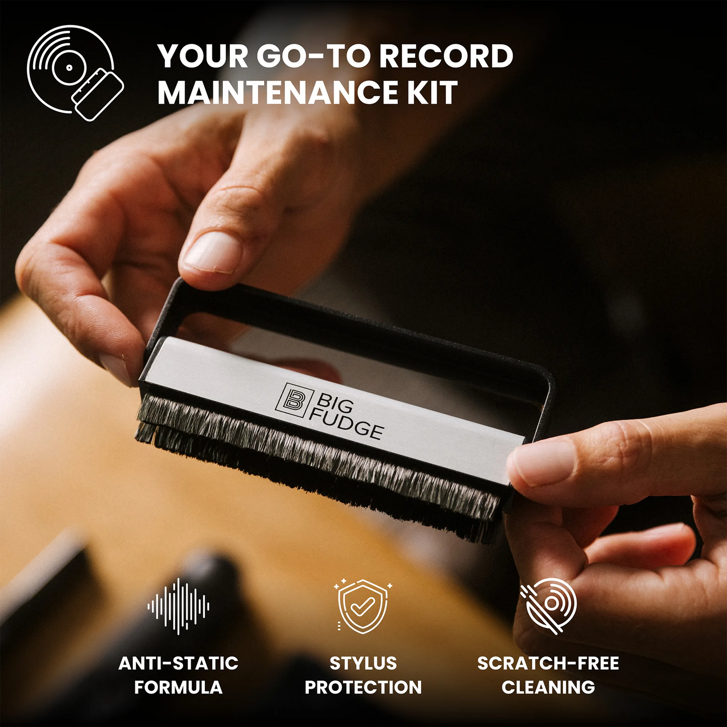 A close-up of a person holding a record cleaning brush labeled BIG FUDGE, with marketing text reading 'YOUR GO-TO RECORD MAINTENANCE KIT' and feature icons for anti-static formula, stylus protection, and scratch-free cleaning.