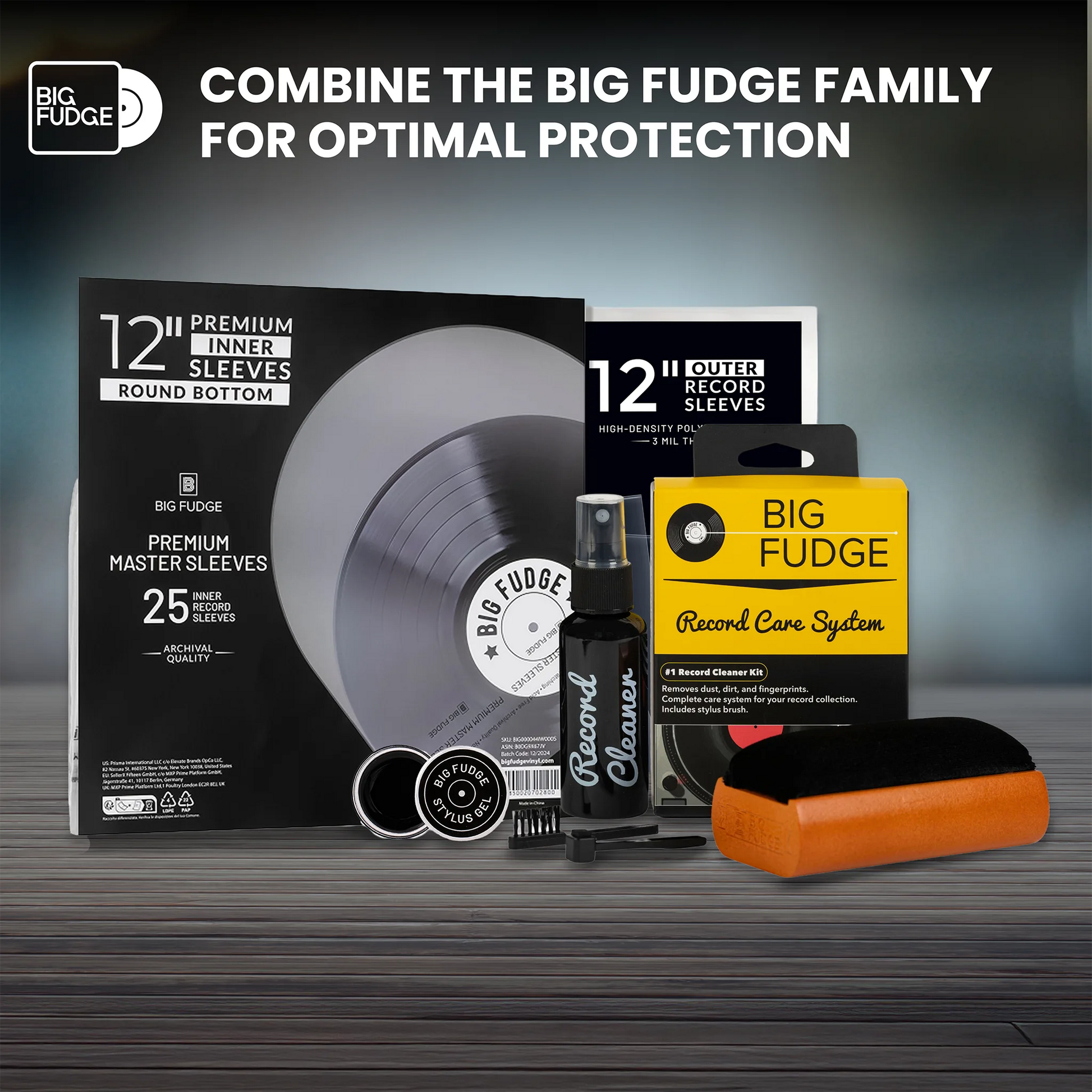 Big Fudge record care and protection set arranged on a dark wood surface against a dark gray gradient background. The set includes a black vinyl record sleeve package, a black spray bottle labeled 'Record Care', a yellow 'Record Care System' box, a black-and-orange cleaning block, and two small round black accessories.