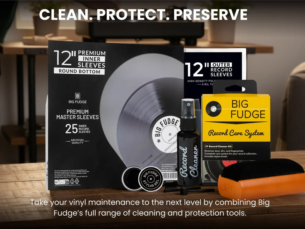 Big Fudge vinyl record care and protection set displayed on a wooden table, including a 12-inch premium inner sleeve round bottom box, a 12-inch outer record sleeve box, a black Record Cleaner spray bottle, a yellow Big Fudge card, and an orange-and-black cloth, with the headline 'CLEAN. PROTECT.