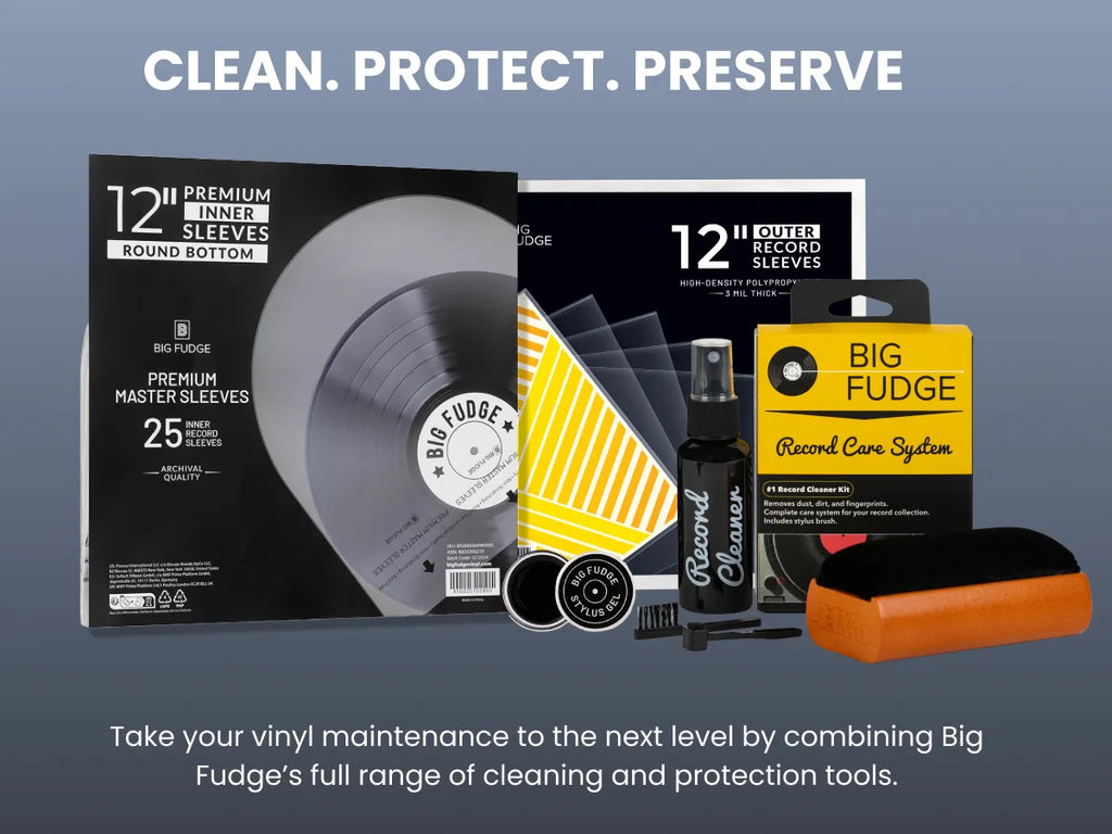 Big Fudge vinyl record care and protection kit displayed on a blue-gray gradient background. The set includes a 12-inch premium inner sleeve round bottom box, a record care system box, a yellow striped cleaning cloth, a black record cleaner spray bottle, a small brush, and an orange-and-black cleaning block.